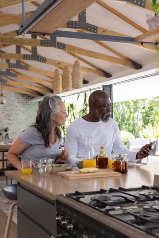 Senior couple leaning over kitchen island sharing smartphone in open-plan kitchen beams