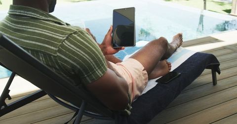 Relaxing by pool with tablet and drink on deck chair, summer remote leisure moment