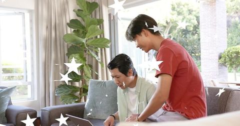 Father and teen son collaborating on laptop in bright living room with gentle star overlays
