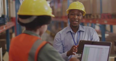 Warehouse supervisor consulting with worker using tablet and laptop in logistics aisle