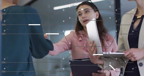Businesswomen Shaking Hands in Modern Office While Holding Tablet and Clipboard