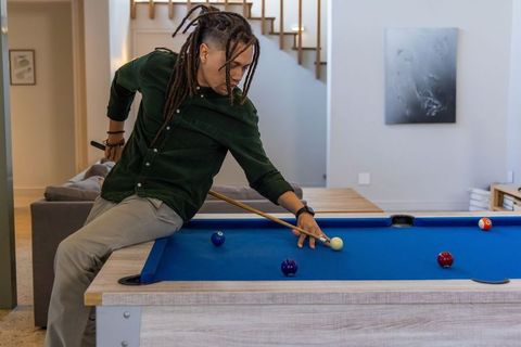 African american man aiming cue on blue-felt pool table in modern minimalist home lounge