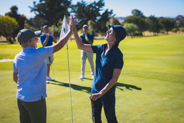 Two happy caucasian senior women at golf course high fiving after their game. golf sports hobby, healthy retirement lifestyle.
