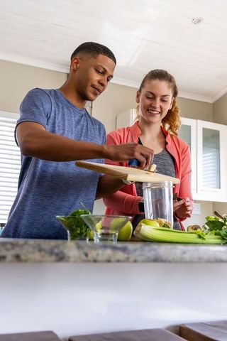 Young couple making healthy green smoothie together in bright modern kitchen