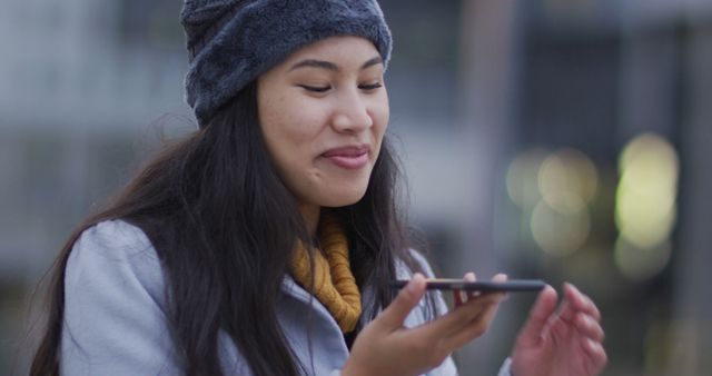 Asian woman using smartphone for voice command in urban environment. Perfect for technology, communication, and urban lifestyle themes. Can be used for marketing campaigns, blog posts, and articles about modern technology and connectivity.