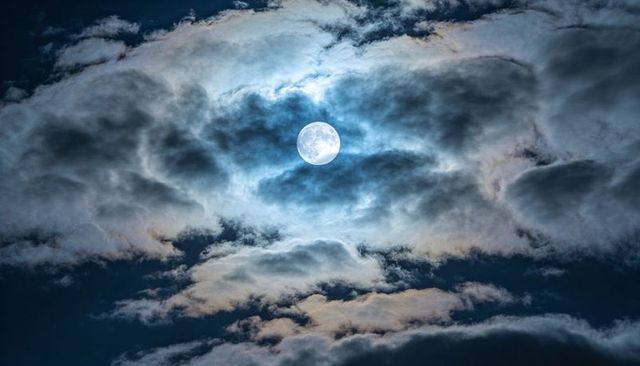 Full Moon Illuminating Layered Clouds with Silver-Blue Glow and Warm-Orange Halo