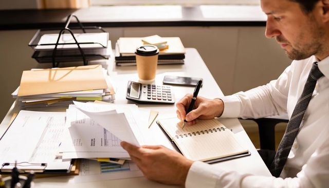 Accountant reviewing financial documents and writing notes at desk with calculator