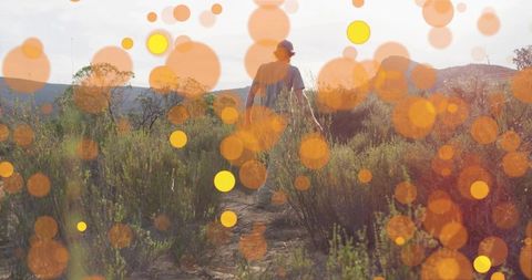Backlit hiker walking sunlit scrub trail with warm bokeh overlay and distant hills