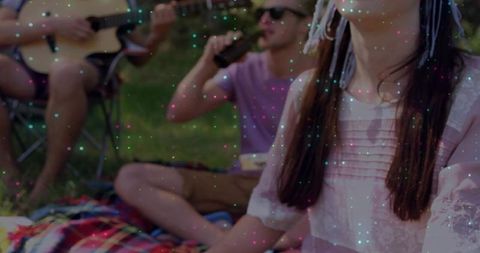Young friends enjoying picnic with guitar and drinks outdoors, woman in pink lace blouse