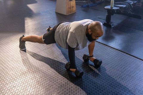 Man performing dumbbell plank on rubber gym floor for core strength and balance training