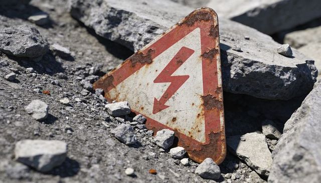 Tilting rusted electrical hazard sign among broken concrete rubble and debris