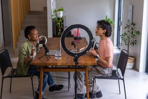 African american woman and asian man recording podcast at dining table using ring light and mics