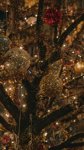Vertical panning video of glittering gold and red Christmas tree ornaments on trunk close-up