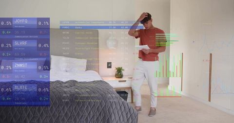 Young man reading financial papers rubbing head in modern bedroom with stock market charts