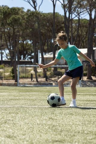 Young girl dribbling soccer ball on sunlit turf near goal practicing skills at local pitch