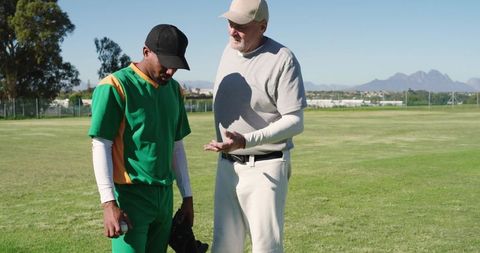 Senior coach guiding african american baseball player during field training session