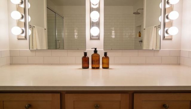 Three amber glass bottles sitting on minimalist bathroom vanity with glowing wall sconces