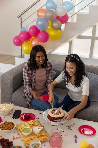 Diverse friends celebrating birthday on couch with velvet cake and balloon garland
