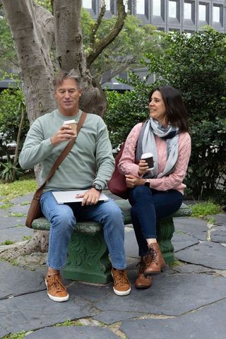 Middle-aged couple enjoying coffee while working on laptop on stone bench in city courtyard
