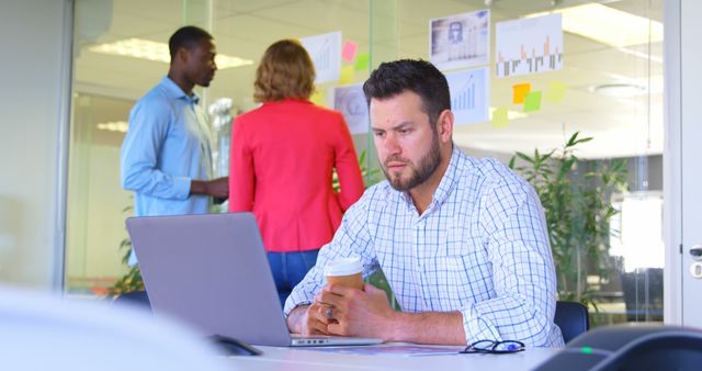 Young Caucasian Businessman Working on Laptop in Modern Office with Coworkers Discussing Charts - Download Free Stock Images Pikwizard.com