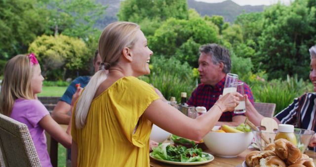 Caucasian woman making a toast turning and smiling during family celebration meal in garden. three generation family celebrating eating outdoors together.