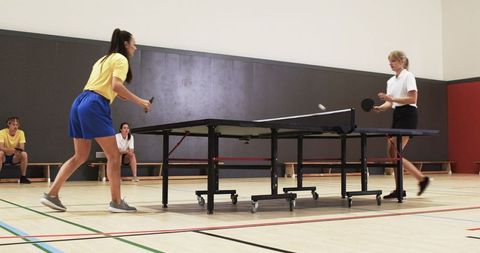 Women engaged in competitive table tennis match in indoor sports hall