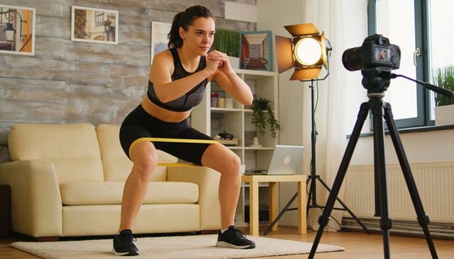 Woman performing resistance-band squats in living room with dslr and studio light