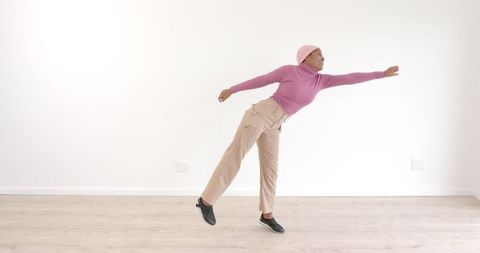 Graceful woman dancing indoors in pink sweater