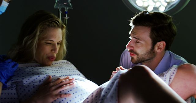 A Caucasian woman in labor is comforted by a Caucasian man, the father, in a hospital setting, with copy space. Their expressions convey a mix of anticipation and concern as they experience the childbirth process together.