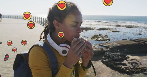 Woman enjoying snack by seaside with heart icons overlay