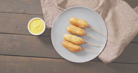 Serving four corn dogs with golden batter on plate with mustard and linen napkin overhead rustic sna