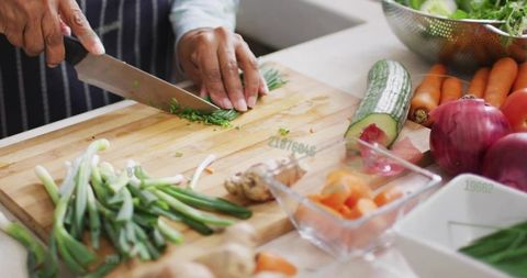 Senior indian woman chopping herbs and vegetables on wooden board in kitchen