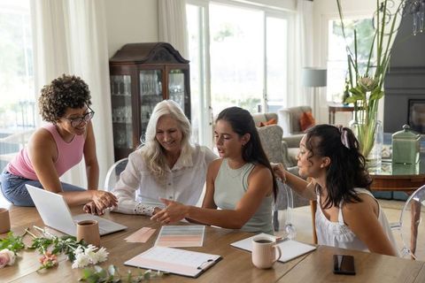 Multigenerational women planning home design using laptop and color swatches at dining table