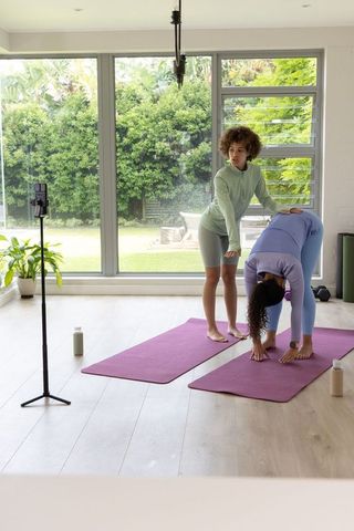 African american yoga instructor guiding participant in forward fold during sunlit at-home practice