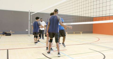 Diverse male volleyball teams shaking hands at net in gym promoting sportsmanship