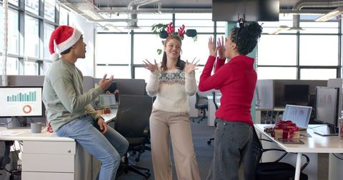 Diverse coworkers celebrating holiday party in modern office wearing Santa hat and antlers