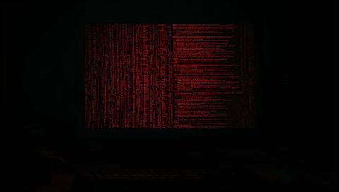 Glowing red terminal code on dark monitor at cybersecurity workstation