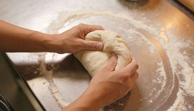 Hands kneading dough on floured stainless counter for artisan bread making
