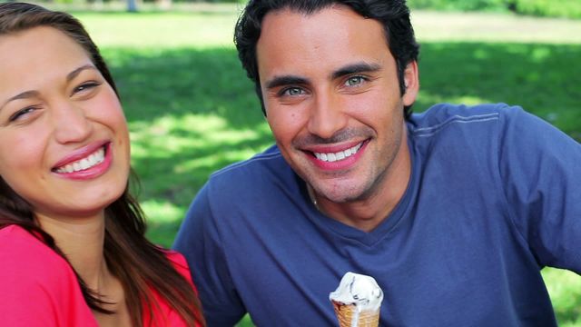 This video shows a cheerful couple enjoying their time together in a sunny park while eating ice cream cones. Perfect for use in marketing materials related to relationships, leisure activities, happiness, summer events, and outdoor fun.