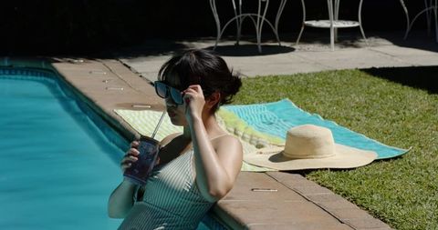 Woman relaxing by poolside with cold drink in sunny backyard