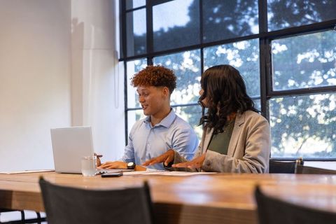 Young diverse coworkers collaborating over laptop in modern bright conference room planning