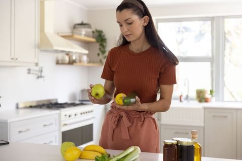 Inspecting fresh fruit on modern kitchen island in dusty rose apron for healthy meal prep