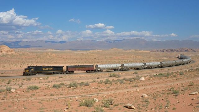 Freight train traveling across arid desert plain with tanker cars and locomotive