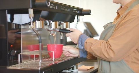 Barista pulling espresso into red cup using commercial espresso machine at cafe counter