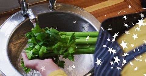 Washing celery under running faucet in kitchen sink with navy apron and star overlay