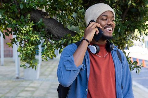 Smiling african american man talking on phone wearing beanie and headphones in urban walk