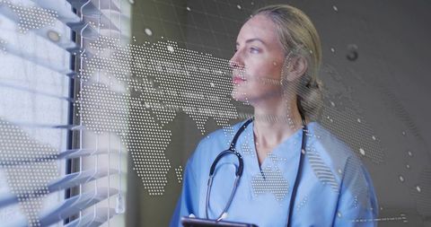 Nurse gazing through blinds holding tablet with world map overlay for telehealth