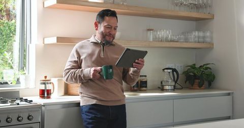 Mature Man Enjoying Morning Coffee Reading Tablet in Bright Kitchen