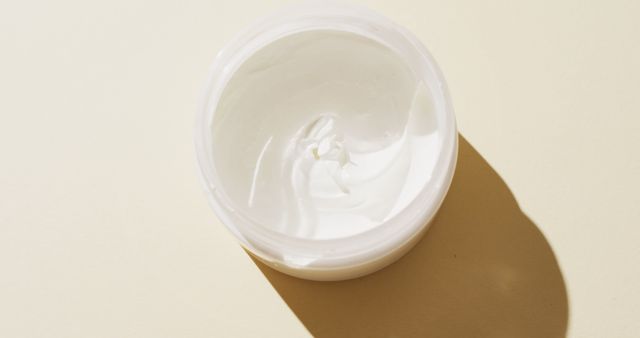 This image shows an open jar of white cream against a beige background. Ideal for use in articles or advertisements related to skincare, beauty products, moisturizer reviews, and personal care routines. Can also be used on websites or blogs focused on beauty and self-care.