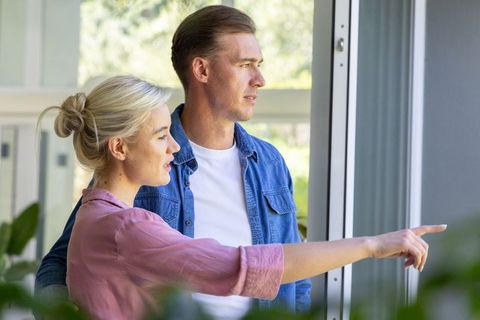 Young couple looking out through sliding glass door pointing at garden in modern home
